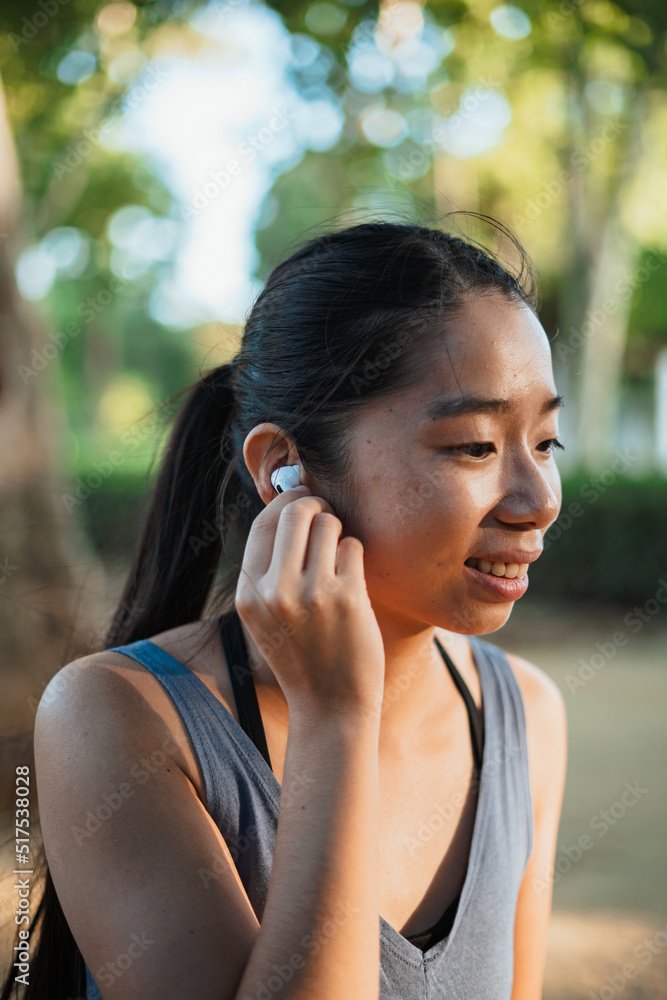 Shot of asian fitness woman putting a wireless earbud in to listen to music while she runs Shot of asian fitness woman putting a wireless earbud in to listen to music while she runs