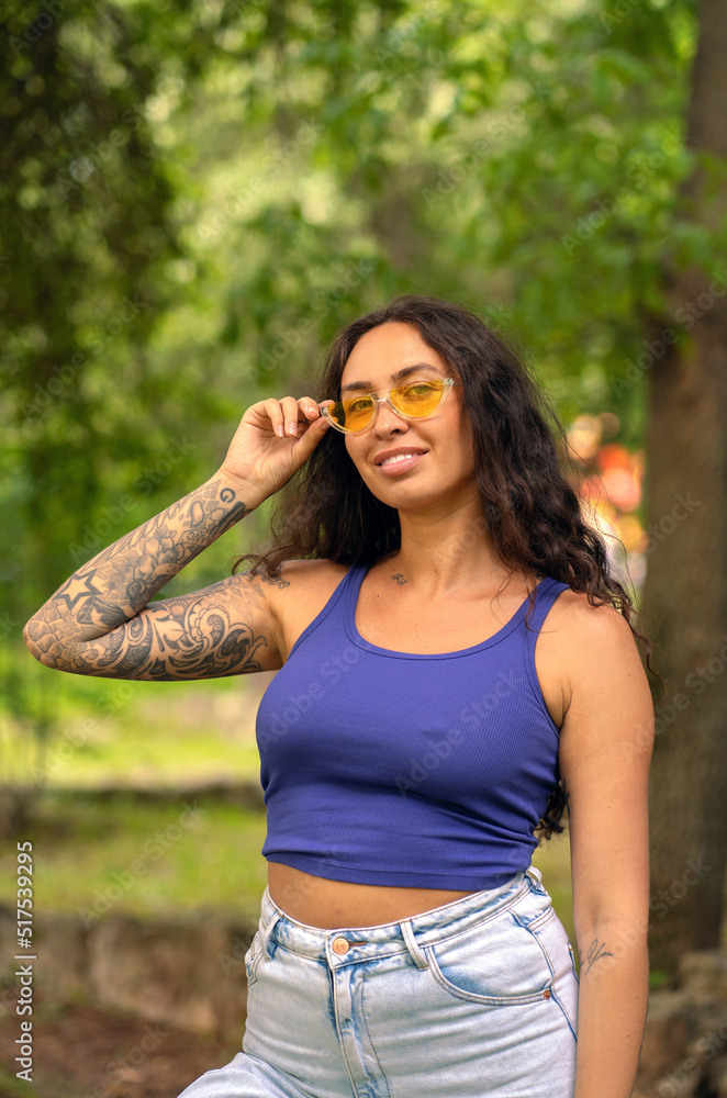 Beautiful girl with tattoos in yellow sunglasses in the summer in the park Beautiful girl with tattoos in yellow sunglasses in the summer in the park