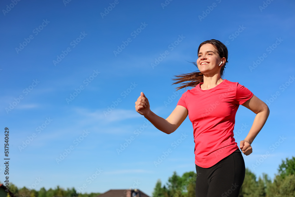 Young woman listening to music while running outdoors in morning. Space for text