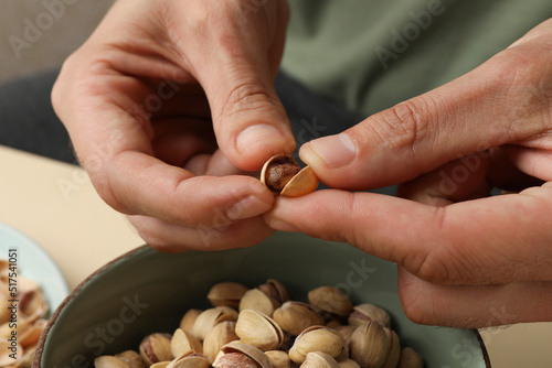 Woman opening tasty roasted pistachio nut at table, closeup