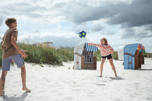 Happy teen children joyful playing voleyball on white summer beach at holidays
