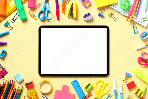 Distance learning, e-learning, online lesson concept. Flat lay tablet mockup with blank screen and colorful school supplies on yellow background. Top view. Copy space.