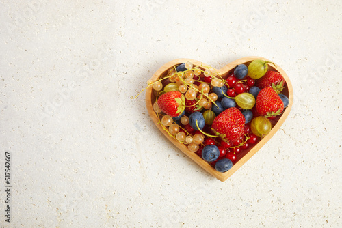 Berries mix in in a heart shaped bowl on travertine background