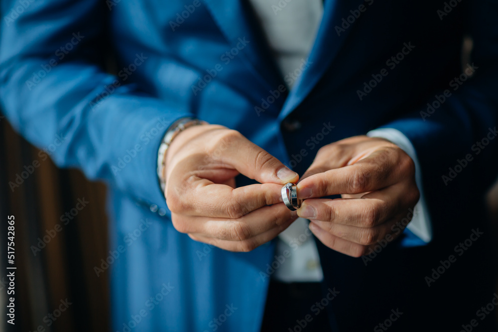 wedding rings in the hands of the groom, the groom in a blue suit