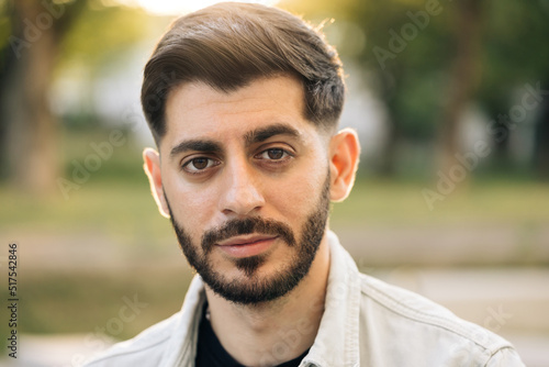 Close up of face young caucasian bearded handsome man looking at camera serious attractive beautiful male stand on street city lifestyle summer guy city outdoors