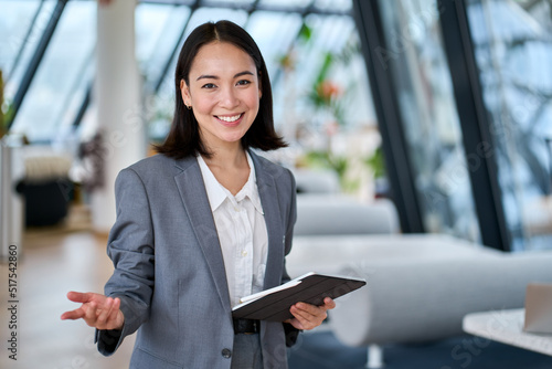 Happy young Asian saleswoman looking at camera welcoming client. Smiling woman executive manager, secretary offering professional business services holding digital tablet standing in office. Portrait