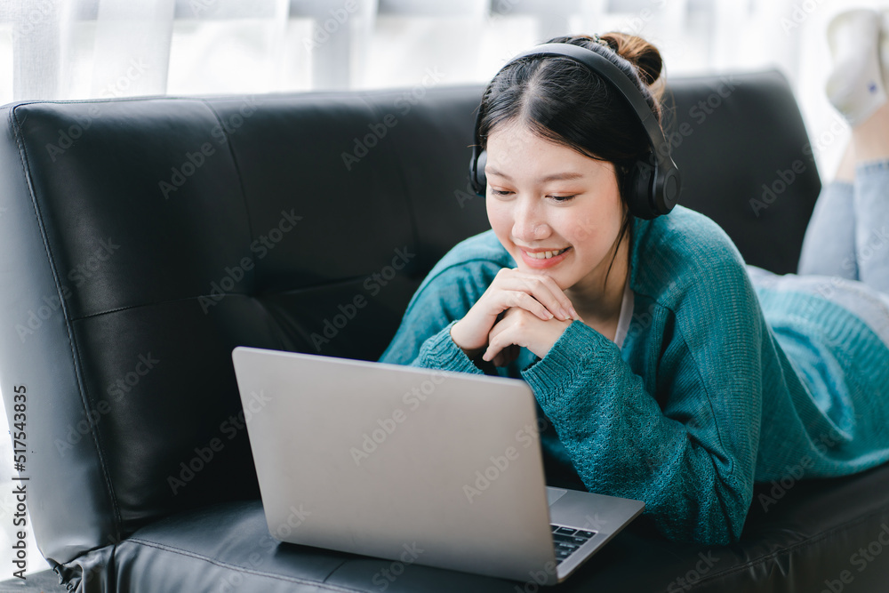Naklejka premium Smart and positive Asian female freelancer or female college student sitting on sofa with laptop. Study from online webinars or home courses. Video calling and chatting
