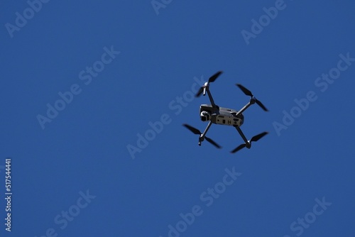 A drone flys overhead against a blue sky.