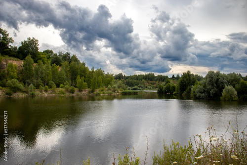 View of the lake on a cloudy day. Heavy clouds over the lake in summer. Reflection of the coast in the water on a summer day 