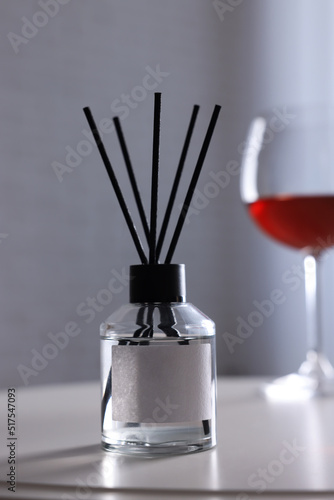 Reed diffuser and glass of wine on white table indoors