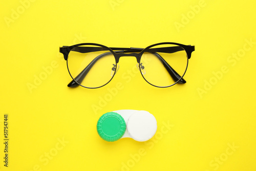 Case with contact lenses and glasses on yellow background, flat lay