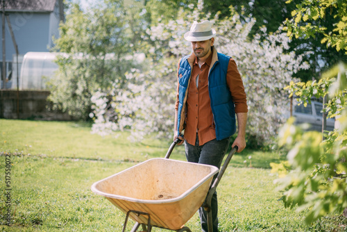 Portrait of a young farmer, a gardener with a garden cart on a plot of land in spring.