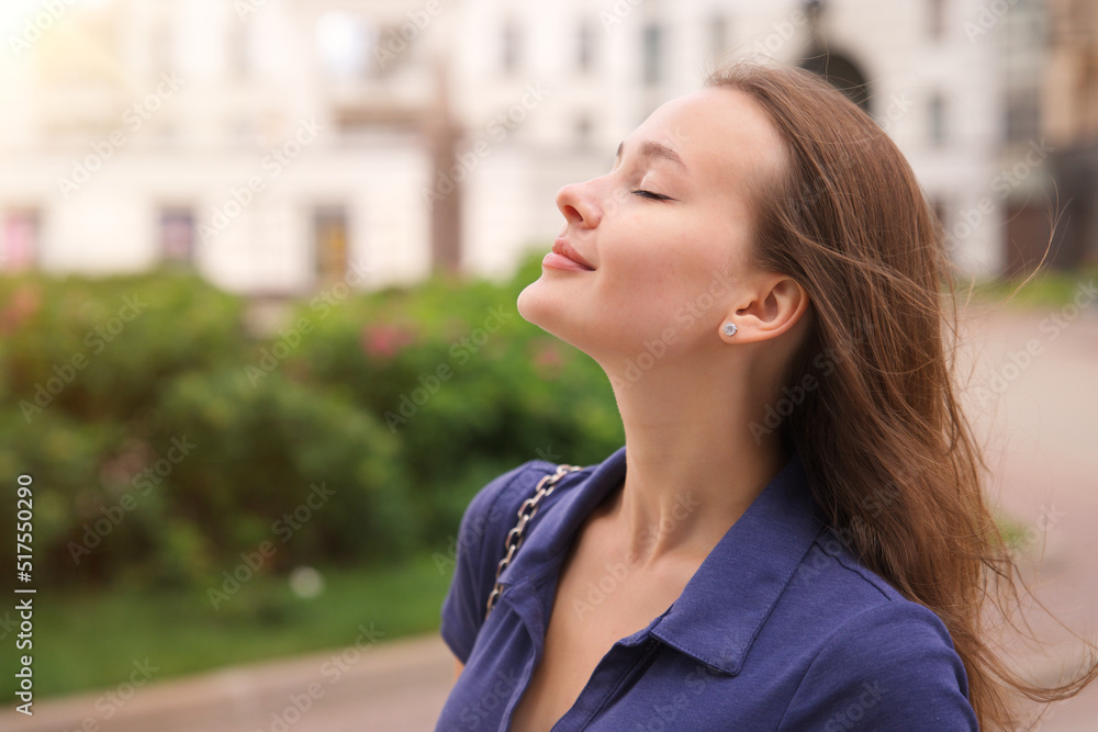 Portrait of beautiful attractive happy girl young European woman is enjoying good summer sunny day in the city, yard or park with eyes closed, breathing deeply deep fresh air smiling Portrait of beautiful attractive happy girl young European woman is enjoying good summer sunny day in the city, yard or park with eyes closed, breathing deeply deep fresh air smiling