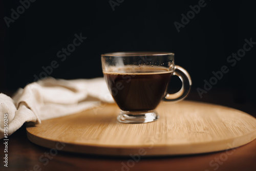 Taza de café, desayuno, taza de vidrio encima de bandeja de madera, en mesa de café de madera, con fondo oscuro, fondo negro, close-up