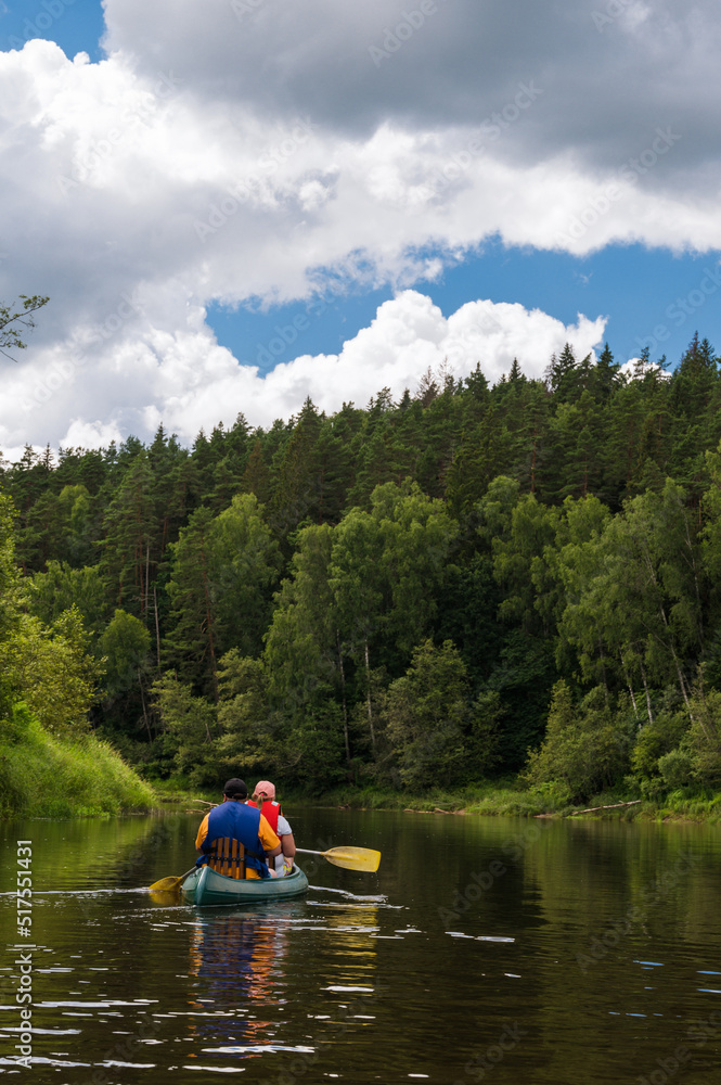 Canoeing on Gauja river at cloudy day. Stormy sky. Pines on shore. Two people in boat.