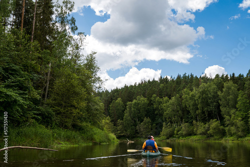 Canoeing on Gauja river at cloudy day. Stormy sky. Pines on shore. Two people in boat.