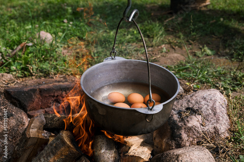 A close-up of eggs being boiled in a pot hung over a fire. Food in hike. Outdoor cooking.