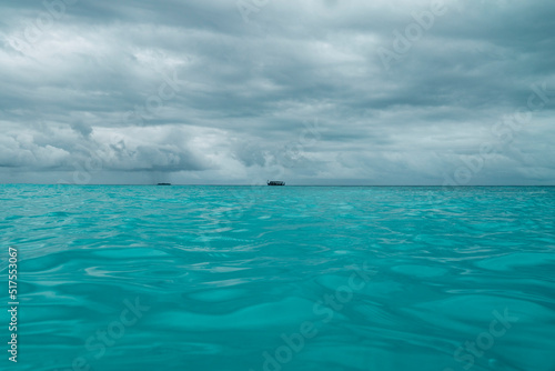 Traditional Maldivian Dhoni Boat passes by on the turquoise blue sea horizon on a stormy day - Wide © Mustard Assets