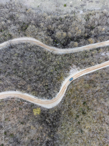 Top-down view of two roads in the middle of a forest, with a blue car passing by
