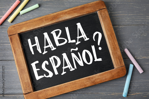 Chalkboard with text HABLA ESPANOL? (DO YOU SPEAK SPANISH?) on wooden background photo
