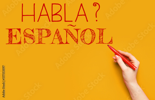 Hand writing text HABLA ESPANOL? (DO YOU SPEAK SPANISH?) on orange background photo
