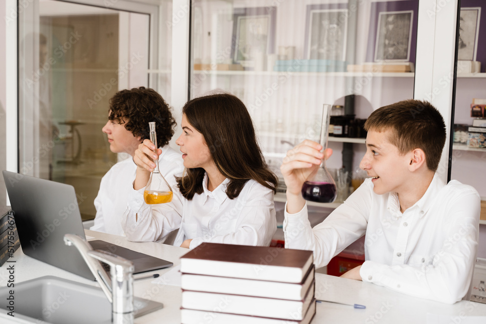 Pupils holding flasks with liquid for experiments in laboratory. Education concept. Group of pupils studying chemistry lesson in school. Pupils holding flasks with liquid for experiments in laboratory. Education concept. Group of pupils studying chemistry lesson in school.