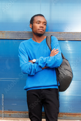 Bored guy wearing a blue sweater and carrying a backpack stands at a bus stop waiting for a bus 