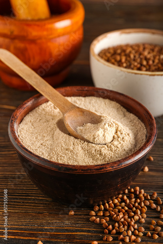 Bowl of flour with spoon and buckwheat grains on dark wooden background, closeup