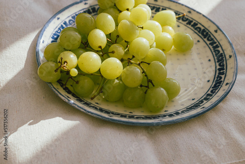 Fresh grapes in sunlight on ceramic plate. Healthy food aesthetics. Summer fruits in light on soft linen background. Summertime in countryside, moody banner