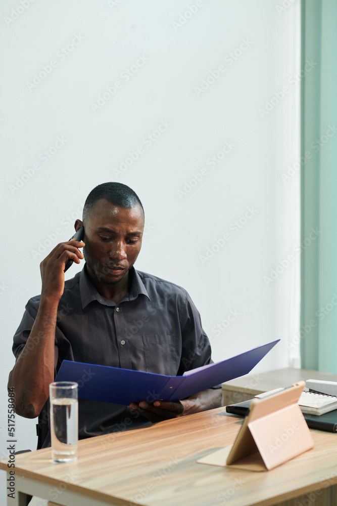 Serious frowning Black businessman talking on phone when reading details of contract Serious frowning Black businessman talking on phone when reading details of contract