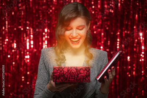 Surprised woman opening christmas gift box with magic shining light on red tinsel background photo