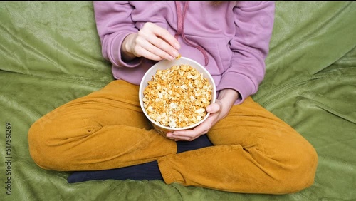 Clode up view on girl or woman holding a popcorn while watching a movie in the living room. photo