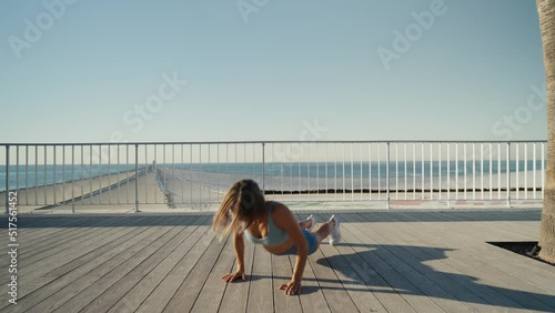 Sportswoman workout outdoor on seaside - she make burpee exercise. High quality 4k footage photo