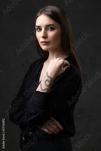 Portrait of a young brunette with long hair in the studio. Dramatic photo in dark colors. A girl with a snake tattoo on her arm.