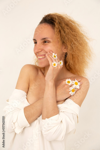 Young caucasian woman applying herbal cream to her face with a smile. Daisies on the hands. The concept of self-care, natural beauty and youth, healthy skin, natural eco-friendly cosmetics. 