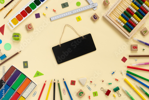 School and office supplies border on beige paper background. Multicolored pencils, paints, plasticine, abacus, pushpins and other school accessories