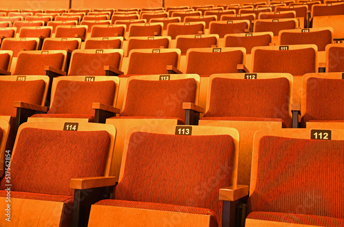 Rows of orange vintage movie theatre seats with numbers on them. © tom