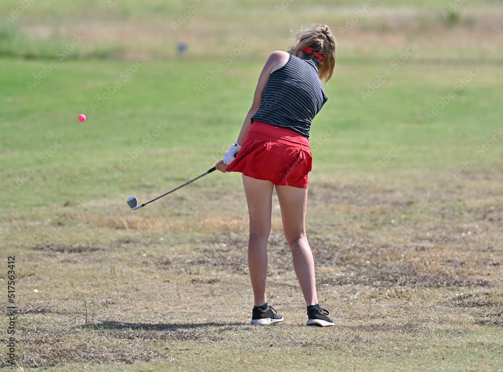 Obraz premium Young girl chipping the golf ball on the green during a golf tournament