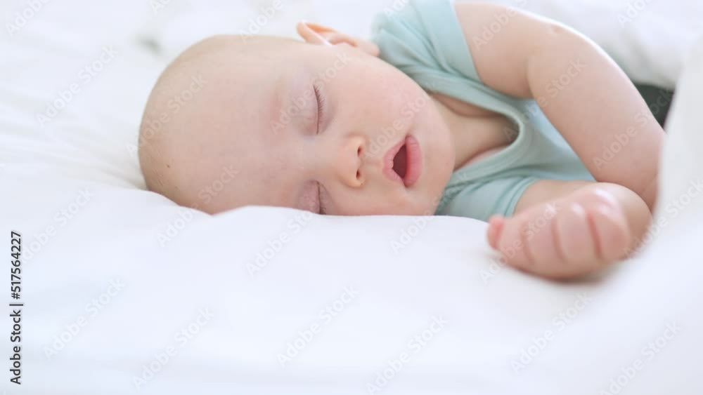 close-up portrait of sleeping infant of three months baby, child lying with closed eyes, opened mouth on white bed. little baby kid moving in dream, while sleeping to napping. asleep child in bedroom close-up portrait of sleeping infant of three months baby, child lying with closed eyes, opened mouth on white bed. little baby kid moving in dream, while sleeping to napping. asleep child in bedroom