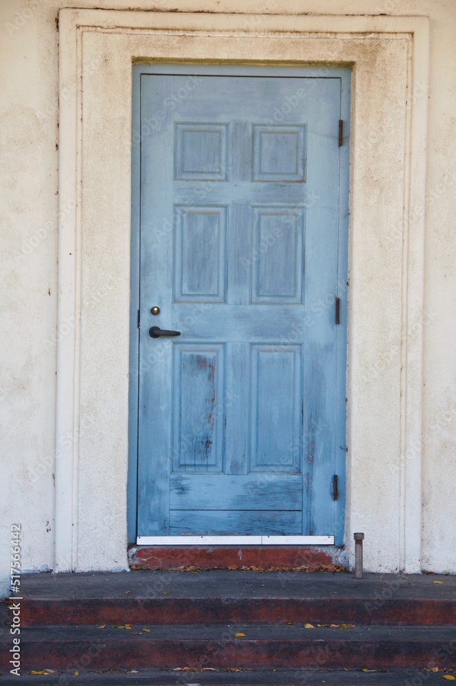 Old blue door with peeling and cracked blue paint against white wall