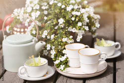 linden tea and porcelain teapot in the sunlight, summer tea party with flowers in the garden