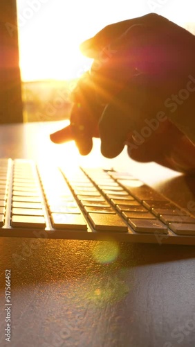 TRZIN, SLOVENIA, 20.5.2022: SLOW MOTION, CLOSE UP: Hands working and typing on computer keyboard in early morning. The rays of sunrise shining over typing fingers and wireless keyboard in home office photo