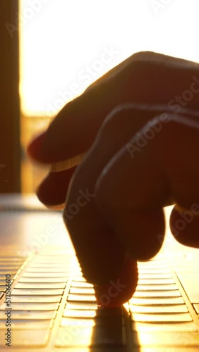 TRZIN, SLOVENIA, 20.5.2022: SLOW MOTION, CLOSE UP: Hands typing on laptop keyboard in early morning sunlight. Sunrise rays shining over fingers of a typing person and laptop keyboard in home office photo