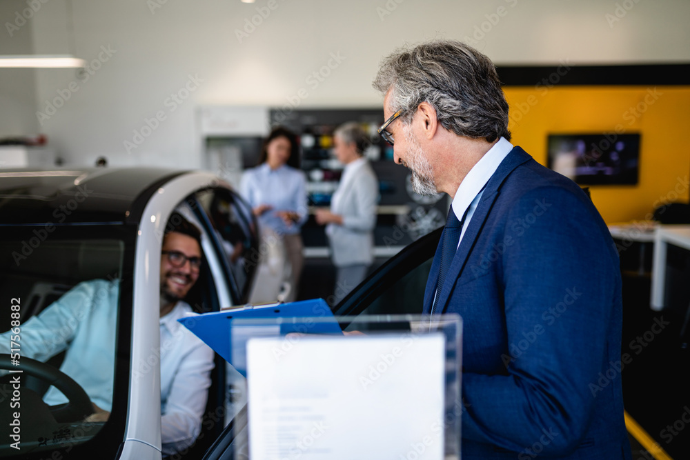 Fototapeta premium Handsome young man buying a new car at the car showroom.