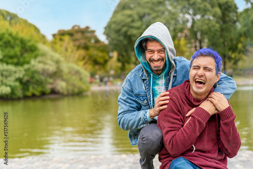 Gay Latino male couple sitting on a bench in a park laughing © Mariano