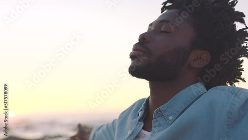 Closeup of an African American man finding inner peace at sunset, tranquil and quiet at a beach with copyspace. Black male meditating and enjoying harmony with nature, zen and calm breathing exercise photo