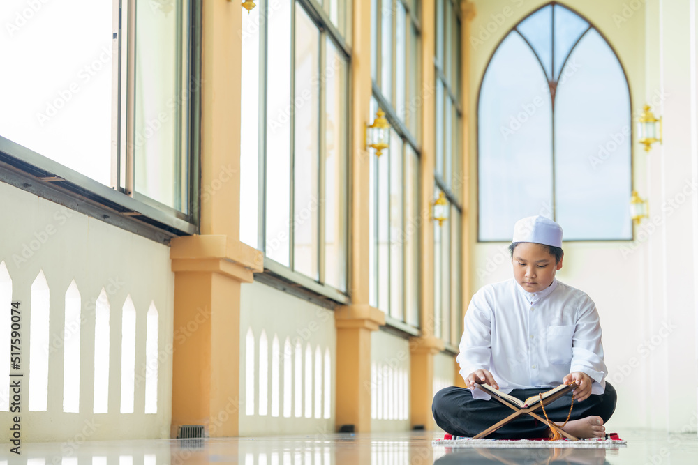 A little Asian Muslim boy is sitting and reading the Quran. The peace in the mosque makes it an energetic atmosphere of faith, with copy space.