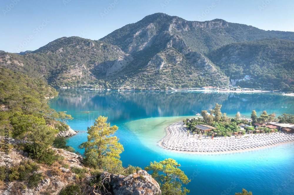 Summer landscape of blue lagoon with white sand surrounded mountains. View from mountain on beautiful beach with umbrellas in Oludeniz, Turkey.