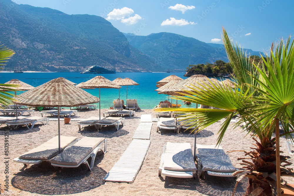 Amazing scenery from coastline with straw umbrallas on sea, Turkey. White yacht near coast. Yacht in the blue lagoon near the sea coast.