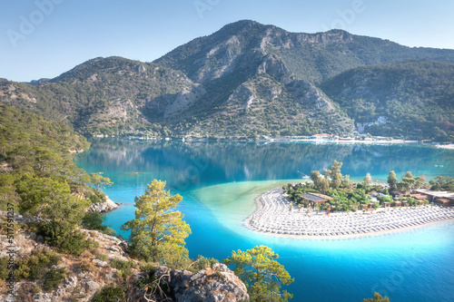 Summer landscape of blue lagoon with white sand surrounded mountains. View from mountain on beautiful beach with umbrellas in Oludeniz, Turkey.
